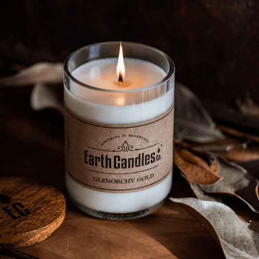 Lit Glenorchy Gold soy candle by Earth Candles Co. in a cut and polished upcycled wine bottle, on rustic timber with dried leaves.