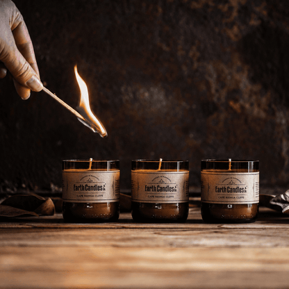 A lit match being held over three unlit Cape Reinga Cliffs soy tealights in cut amber beer bottle bases