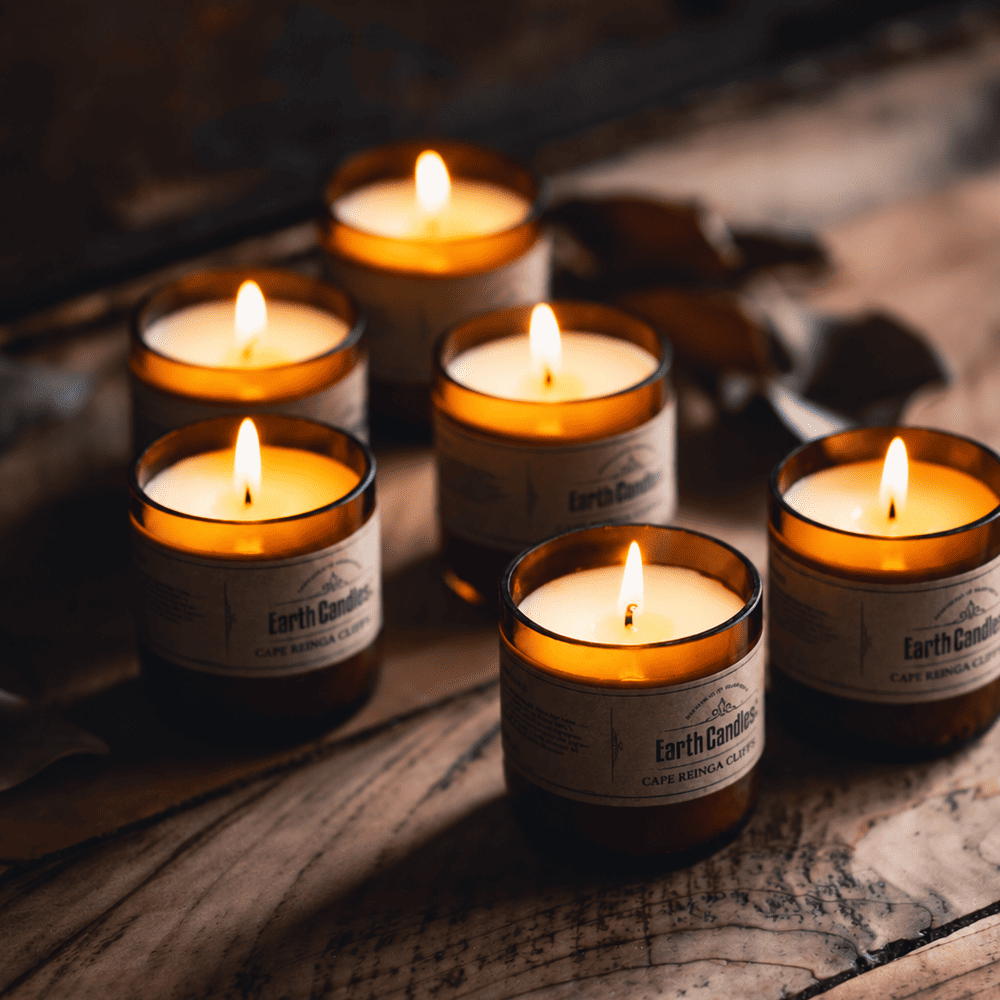 Six Cape Reinga Cliffs soy tealights burning in cut amber beer bottle bases on weathered wood