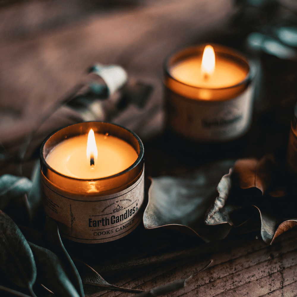 Cooks Candle soy tealights burning in cut amber beer bottle bases among dried leaves