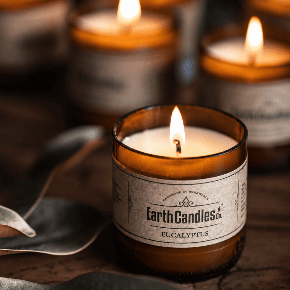 Three Eucalyptus soy tealights burning in cut amber beer bottle bases with dried leaves