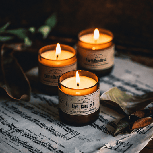 Three Fresh New Zealand Pine soy tealights burning in cut amber beer bottle bases, on sheet music