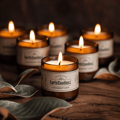Six Glenorchy Gold soy tealights burning in cut amber beer bottle bases with dried leaves