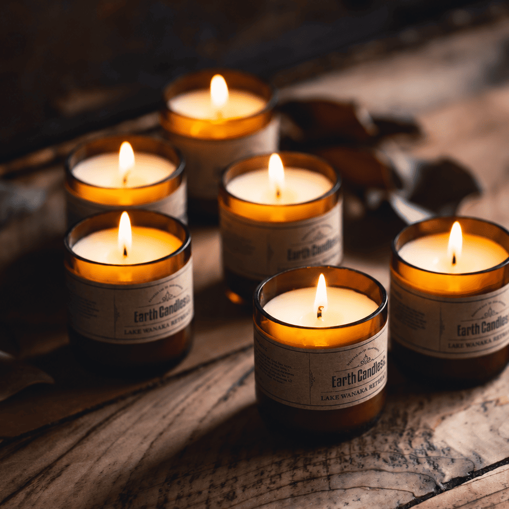 Six Lake Wanaka Retreat soy tealights burning in cut amber beer bottle bases on weathered wood