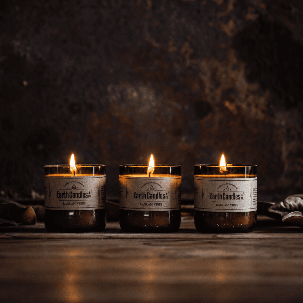 Three Raglan Vibes soy tealights burning in a row in cut amber beer bottle bases