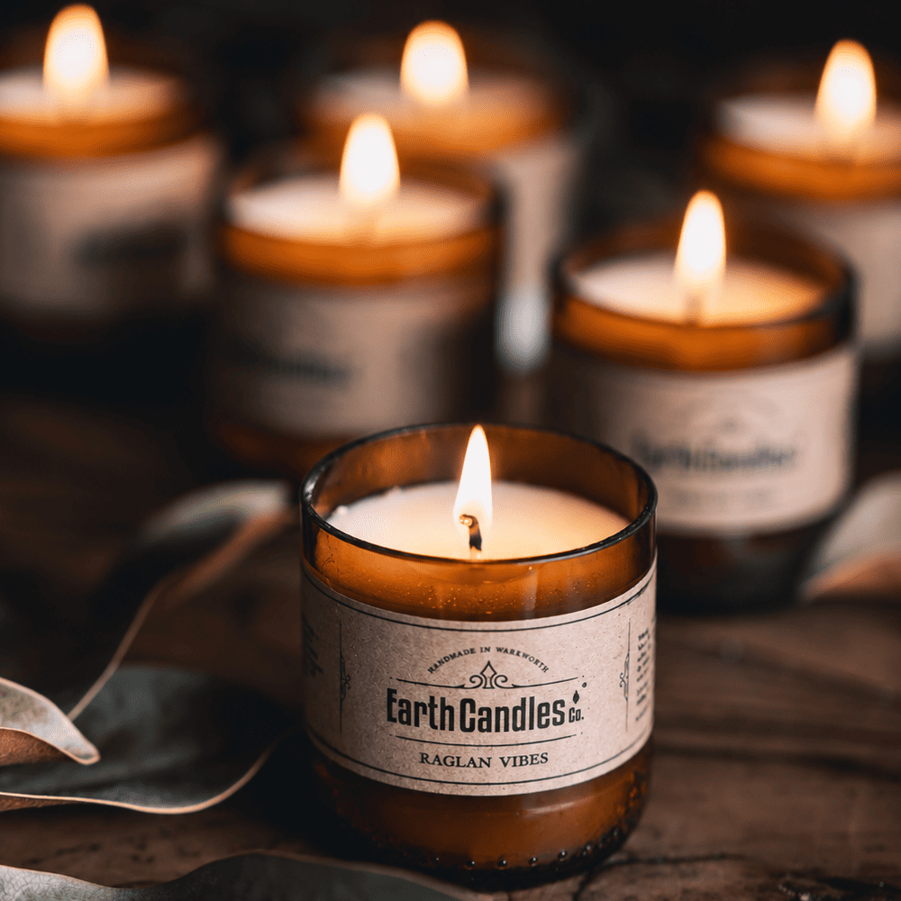 Six Raglan Vibes soy tealights burning in cut amber beer bottle bases