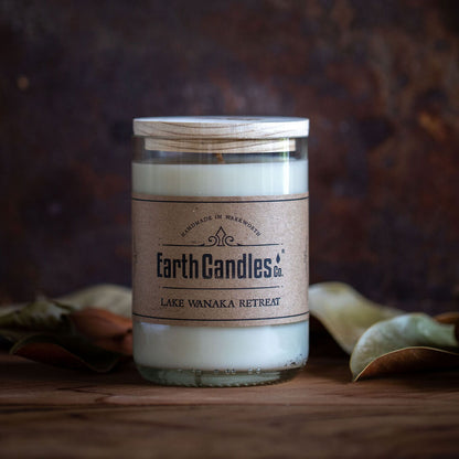 A soy wax candle in a re-purposed clear glass wine bottle with a brown label that reads 'Earth Candles - Lake Wanaka Retreat'.
